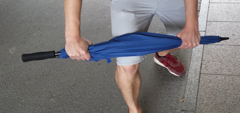 Regenschirm-Stabiliät getestet. Ein Mann hält einen blauen Stockschirm über dem Knie.