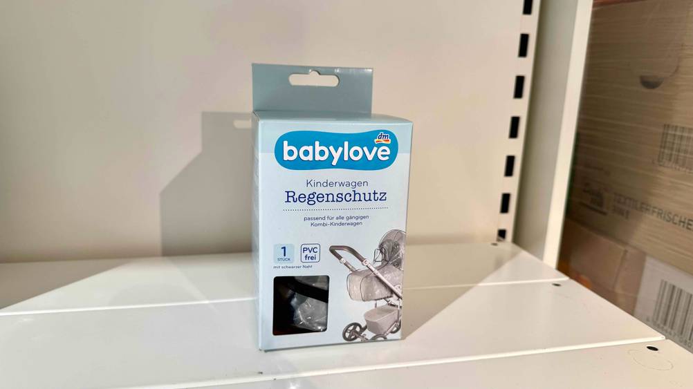 Der originalverpackte Regenschutz Kinderwagen im Test auf einem weißen Regal.