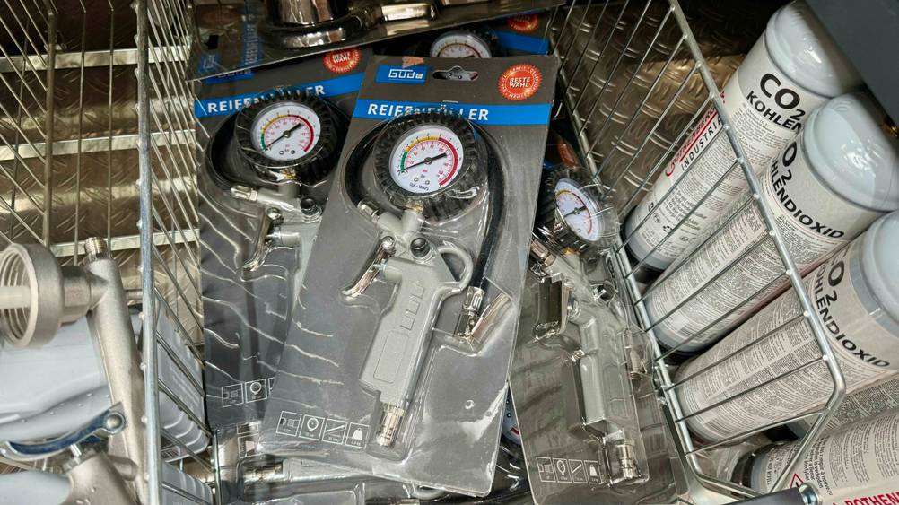 Mehrere originalverpackte Reifenfüller im Test in einem Gitterkorb neben anderen Produkten.
