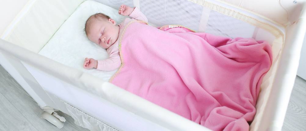 Reisebett-Baby-Test: Baby schläft in weißem Reisebettchen.