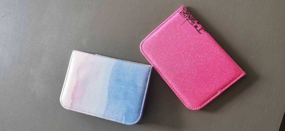 Zwei getestete Reisepasshüllen in verschiedenen Designs liegen schräg auf einer dunklen Fläche.