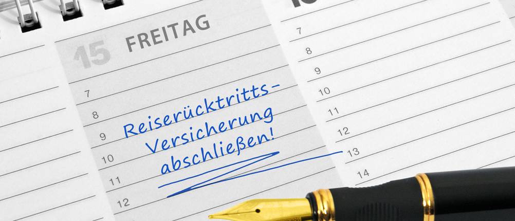 Reiserücktrittsversicherungen-Test: Auf einem Kalender, in dem der Termin zum Abschluss einer Reiserücktrittsversicherung eingetragen ist, liegt ein schwarz-goldener Füller.