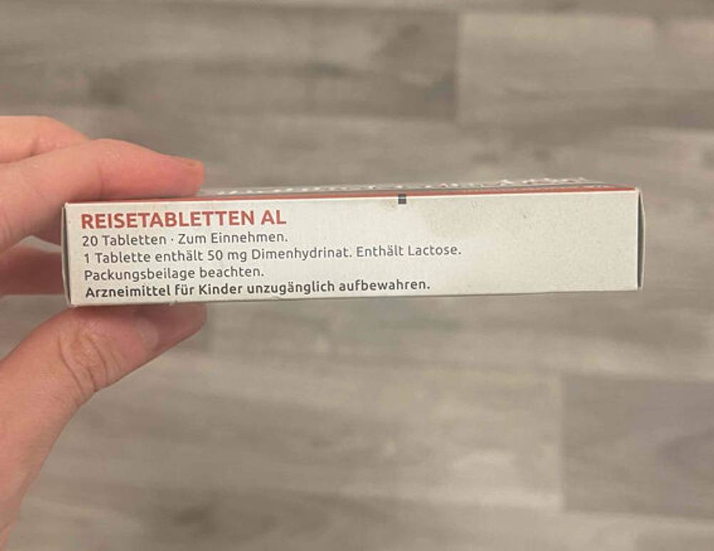 Reisetabletten-Test: Eine Hand hält die Verpackung mit 20 Tabletten inklusive Inhaltsstoff-Beschreibung vor einem braunen Hintergrund.