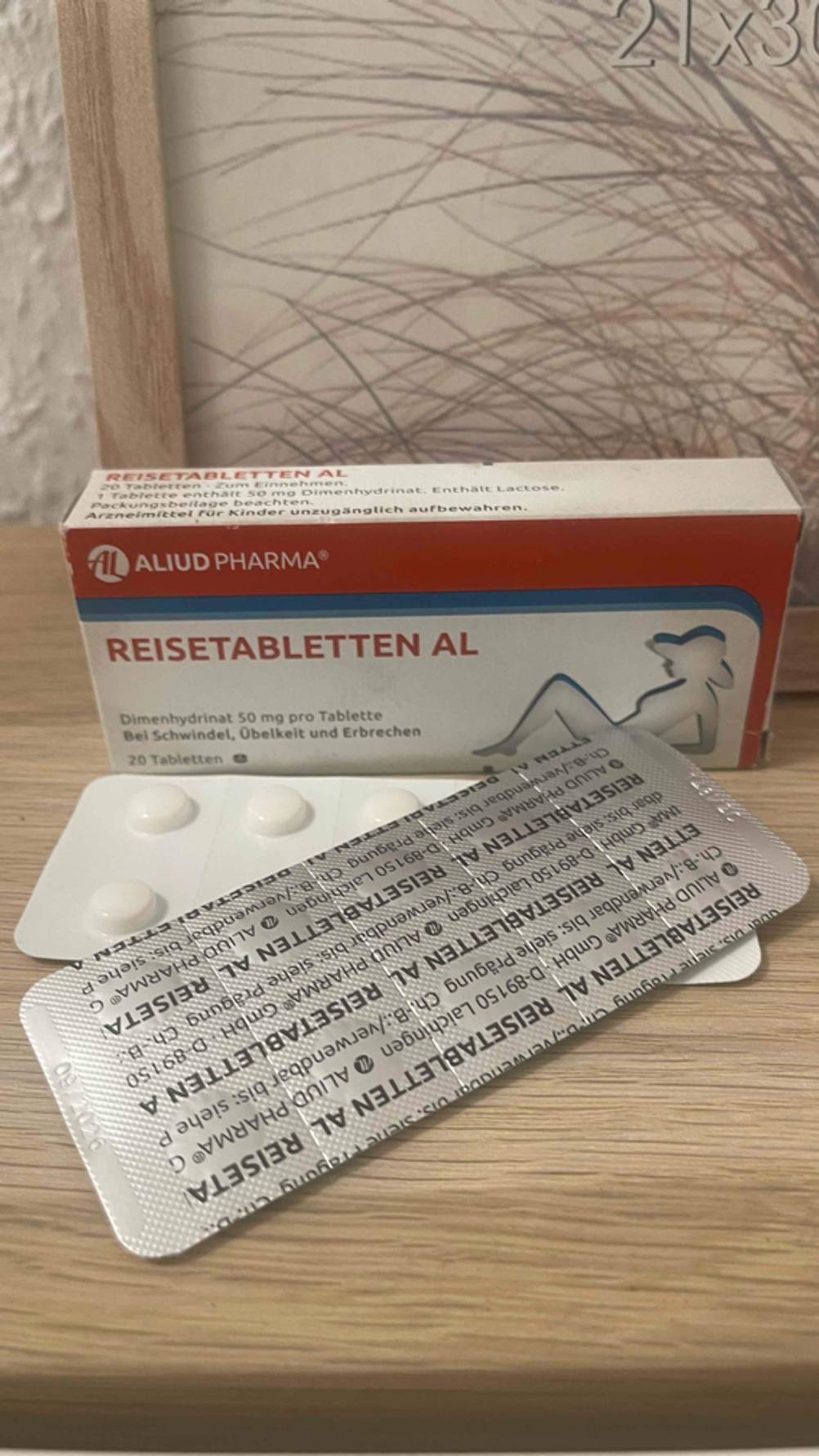Zwei Blister mit den Reisetabletten im Test liegen vor der weiß-rot-blauen Verpackung auf einem Holzregal.