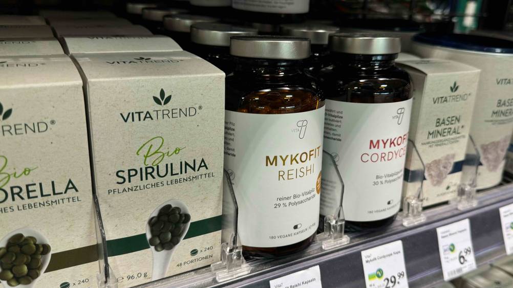 Mehrere Flaschen der Reishi-Kapseln im Test stehen neben anderen Produkten in einem Verkaufsregal mit Preisangaben.