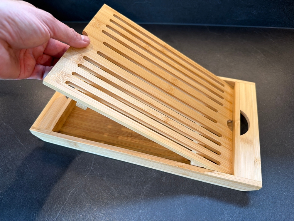 Eine Hand legt den Deckel auf das Relaxdays-Brotschneidebrett