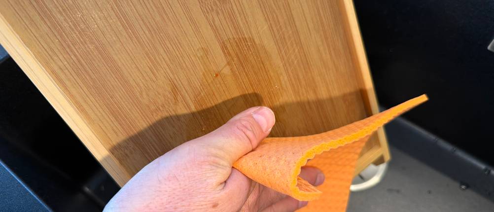 Eine Hand wischt das Relaxdays-Brotschneidebrett mit einem Lappen ab