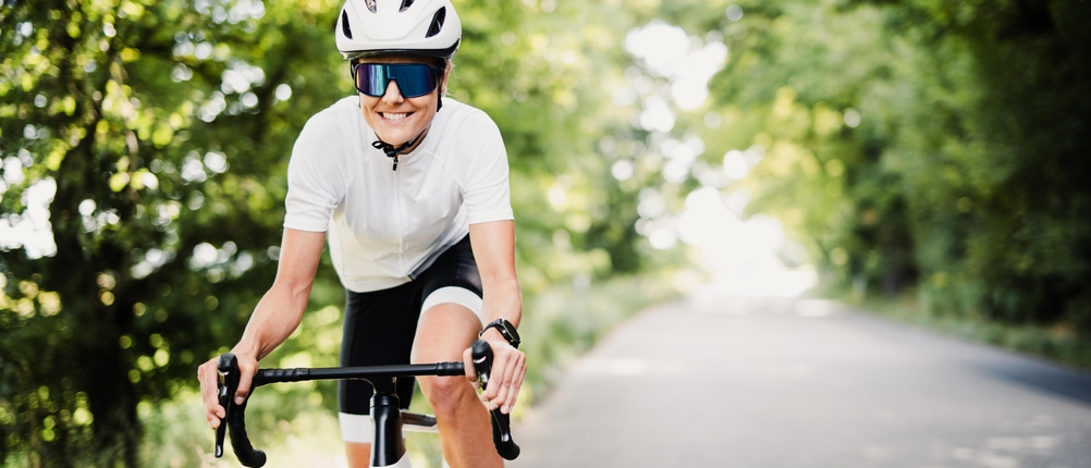 Eine Rennradfahrerin mit Helm und Sonnenbrille fährt auf einer Straße.