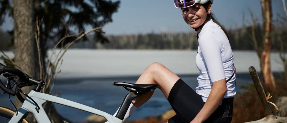 Rennradhelm-Damen-Test: Eine Rennradfahrerin sitzt mit Helm auf dem Kopf auf einem Stein und macht gerade Pause. Ihr Rennrad steht vor ihr.