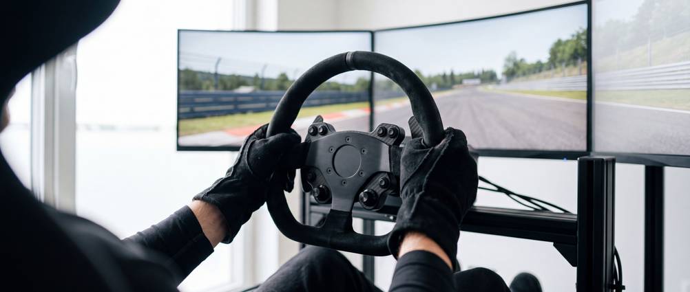 Triple-Screens im Test: Ein Mann mit Handschuhen spielt eine Rennsimulation auf einem Triple-Screen-Setup.