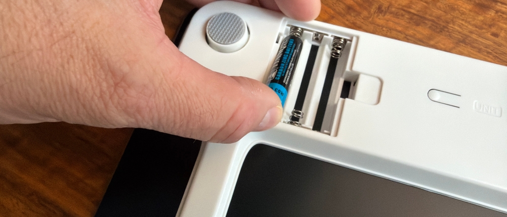 Eine Hand legt die Batterien in die Renpho BG260R.