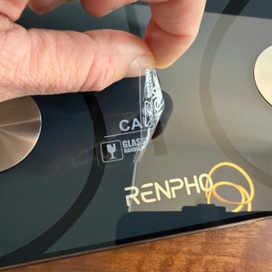 Eine Hand zieht eine Folie von der Renpho ES-CS20M ab