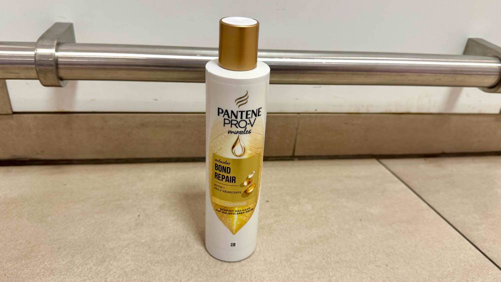 Auf einem beigen Boden steht eine Flasche des Repair Shampoos im Test.