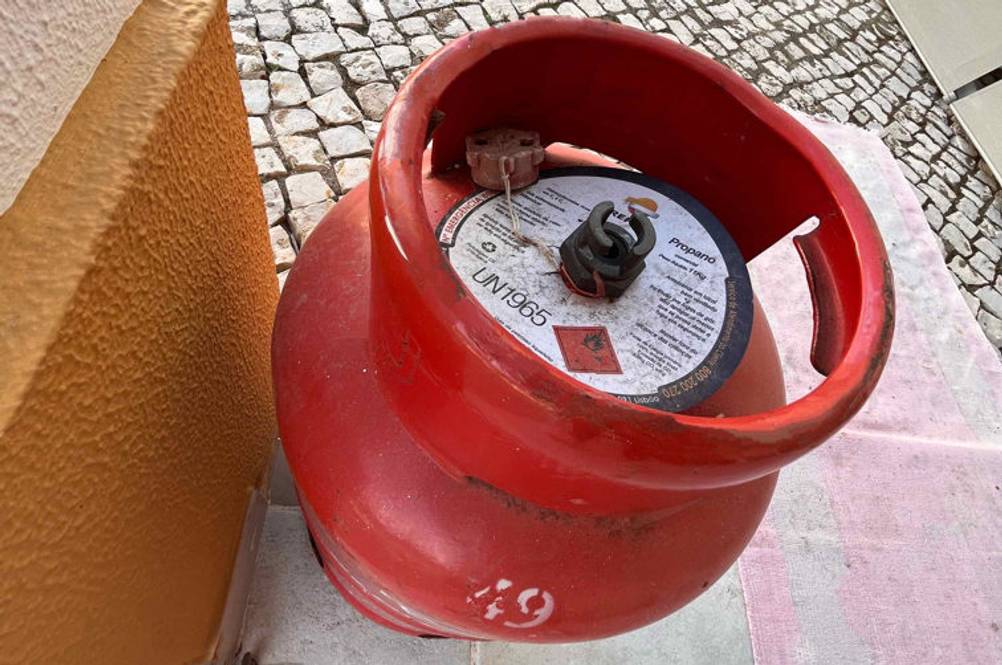 Draufsicht einer roten, getesteten Propangasflasche, einschließlich Ventil und Beschreibungs-Etikett, die sich auf einer Terrasse im Außenbereich befindet.
