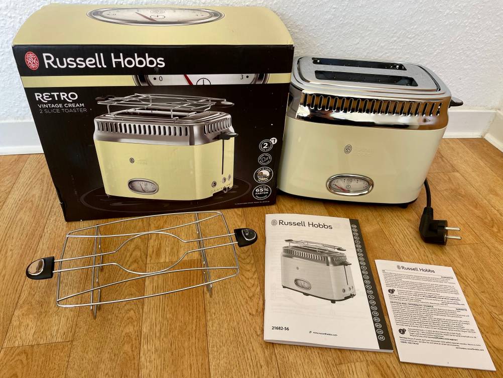 Auf dem Küchentisch befindet sich ein getesteter Retro-Toaster neben der Verpackung und der Bedienungsanleitung. 