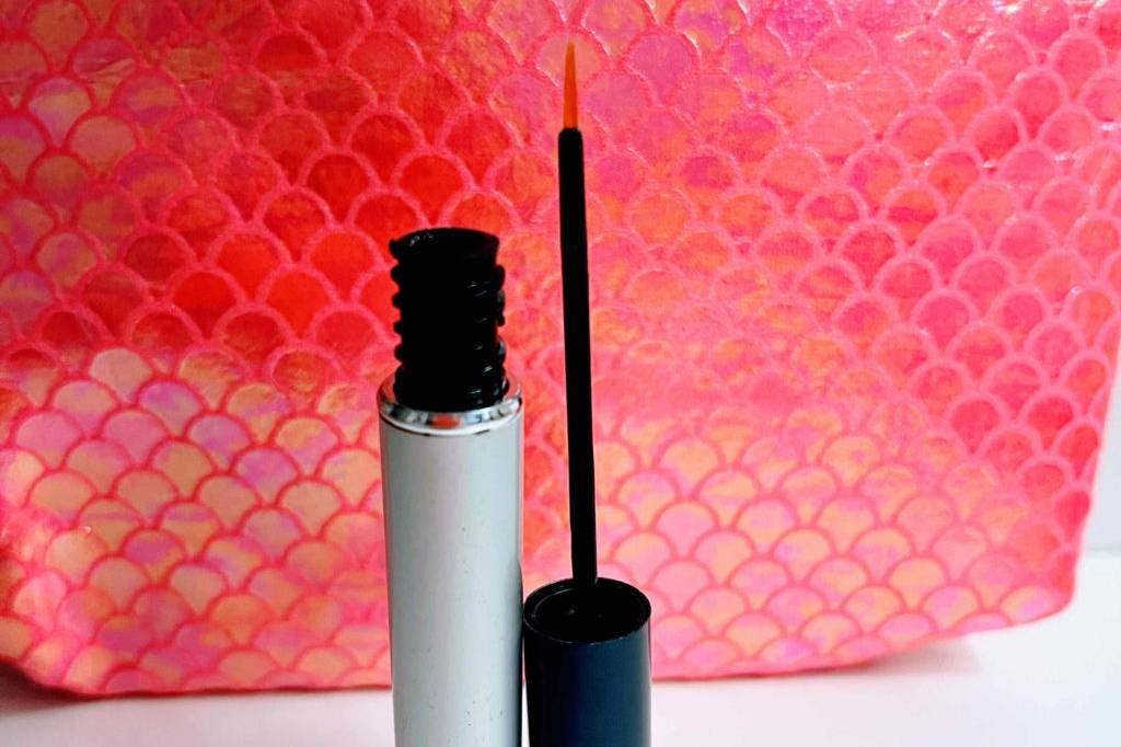 Im Test: geöffneter Behälter Revitalash Wimpernserum steht vor roter Kosmetiktasche.