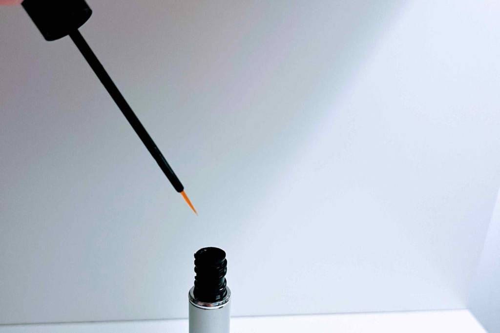 Im Test: Hand hält Pipette über geöffnetes Fläschchen Revitalash Wimpernserum.