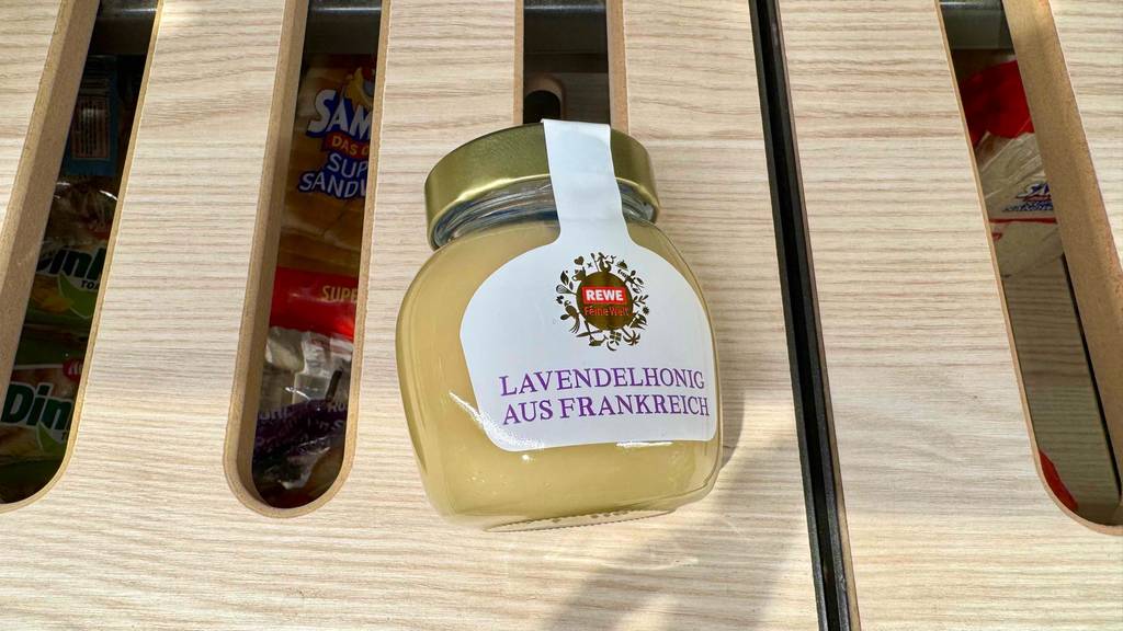 Ein Glas Lavendelhonig liegt zum testen auf einem Holzregal mit Toast darunter.