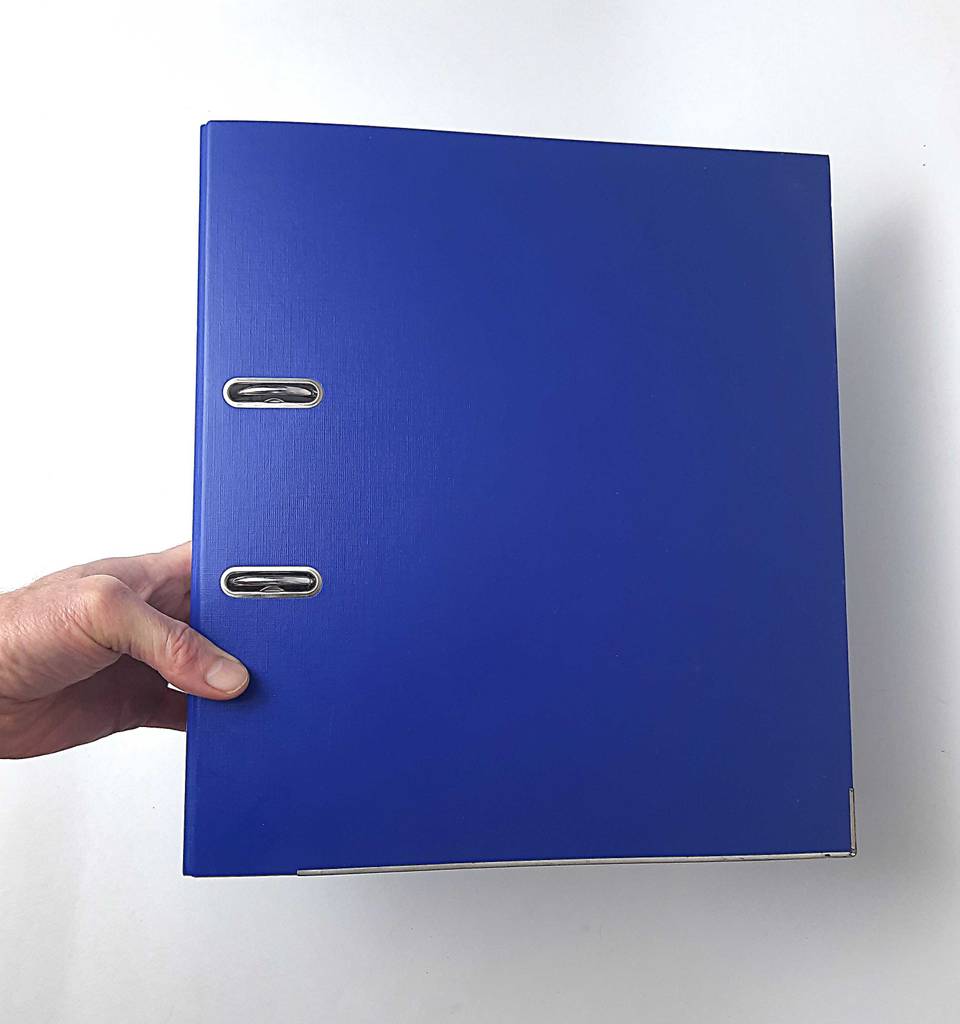Im Test: Eine Hand hält einen blauen Aktenordner vor einer weißen Wand.