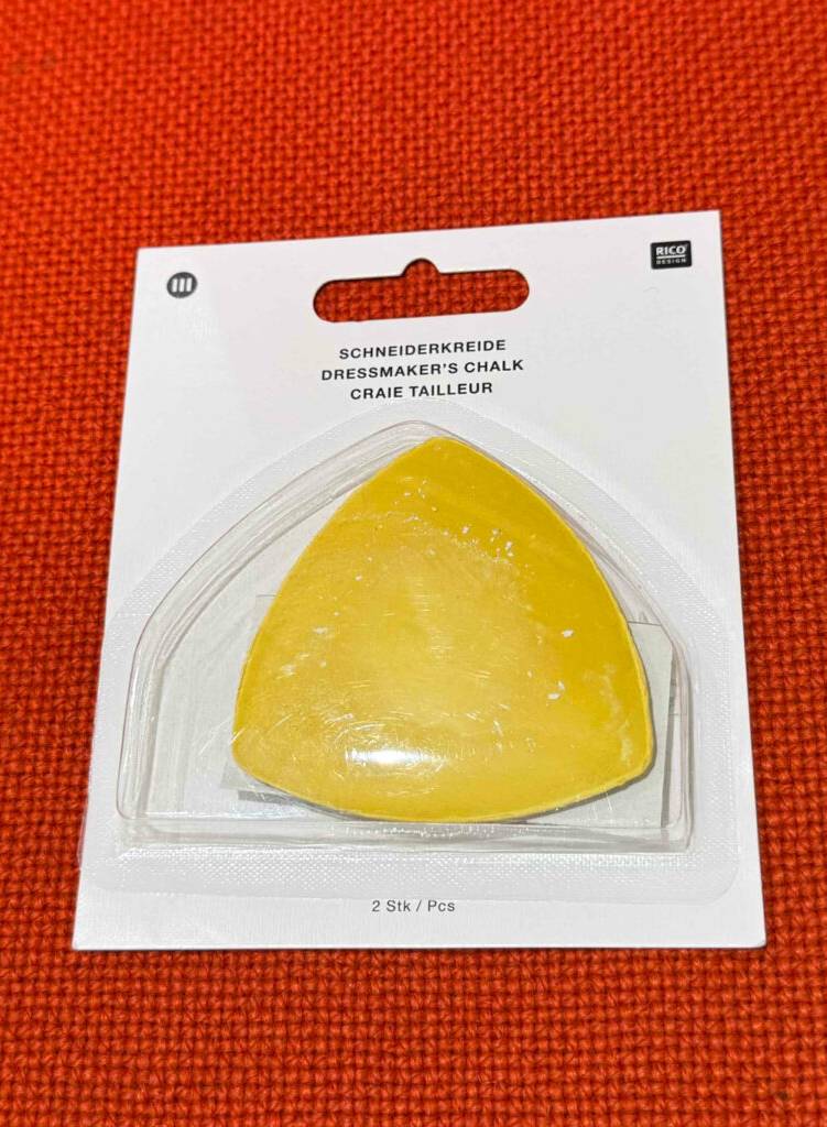 Im Test: Die Schneiderkreide in Gelb liegt in zweifacher Ausführung innerhalb ihrer transparenten Verpackung auf einem roten Stoffgewebe.
