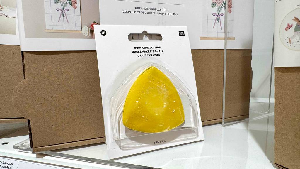 Die getestete Schneiderkreide in Gelb mit drei Ecken innerhalb der transparenten Verpackung befindet sich in einem Handarbeitsbereich im Geschäft.