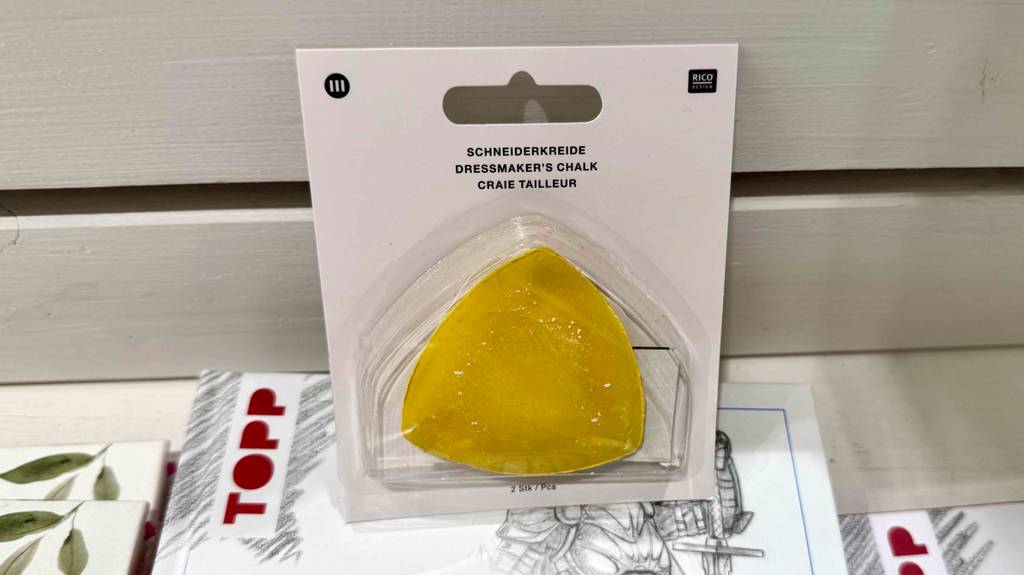Die gelbe, dreieckige Schneiderkreide im Test befindet sich in einer transparenten Verpackung auf einem Schnittmuster.