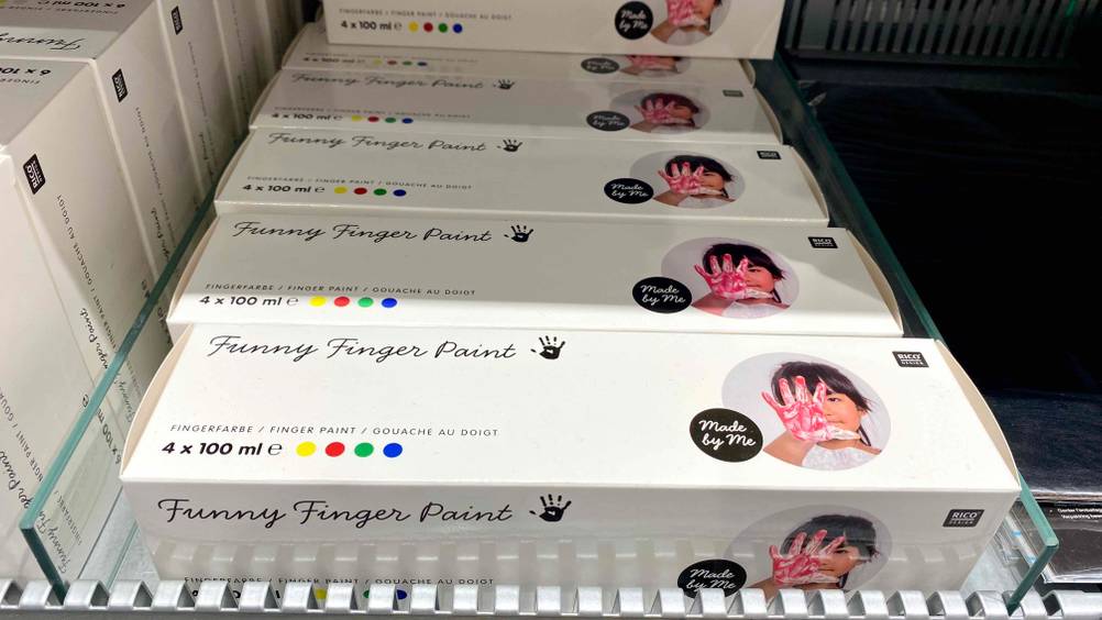 Fingerfarben-Test: mehrere weiße Verpackungen mit Funny Finger Paint Farben liegen hintereinander im Verkaufsregal.