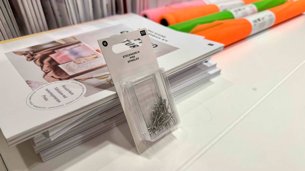 Eine transparente Packung mit Metall-Stecknadeln im Test lehnt an einem Stapel Zeitschriften für Schnittmuster.