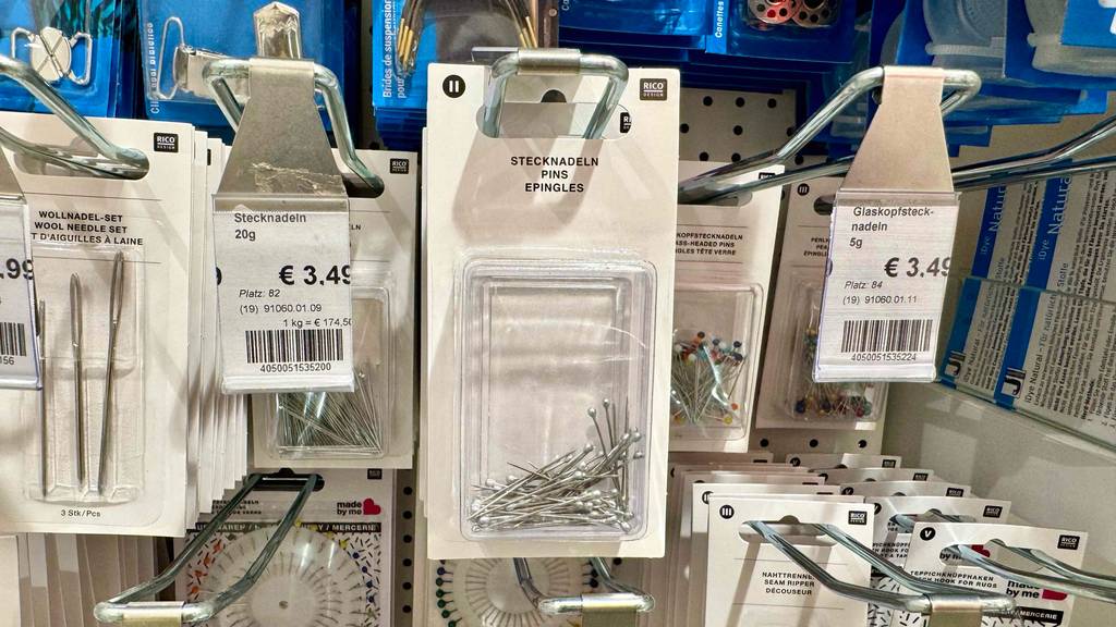 Eine transparente Packung mit getesteten Stecknadeln aus Metall hängt an einem Verkaufsregal zwischen weiteren Nähutensilien.