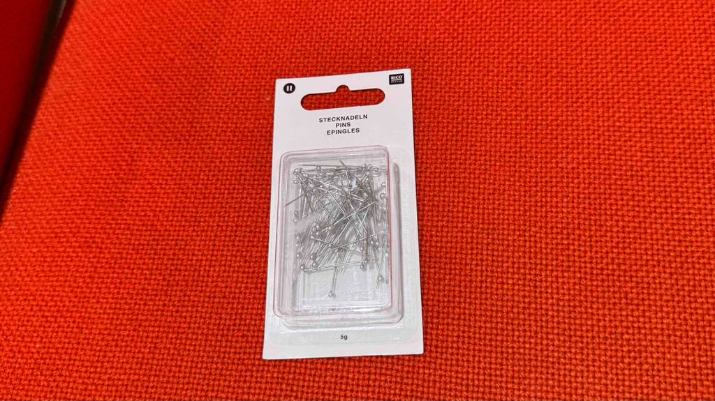 Eine transparente Packung mit getesteten Stecknadeln aus Metall liegt auf einem roten Stoff.