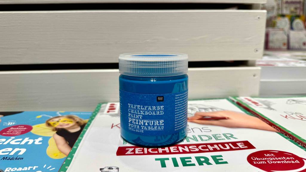 Tafelfarben-Test: Eine Kunststoffdose mit blauer Farbe steht auf einer Malanleitung.