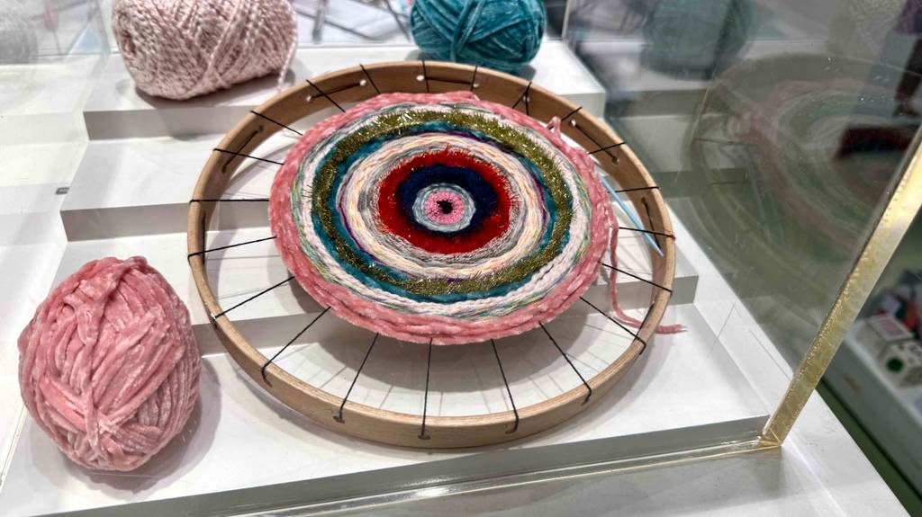 Im Test: Der Webrahmen in runder Ausführung befindet sich inklusive mehrfarbigem Muster in einer Ausstellungsbox hinter Glas.
