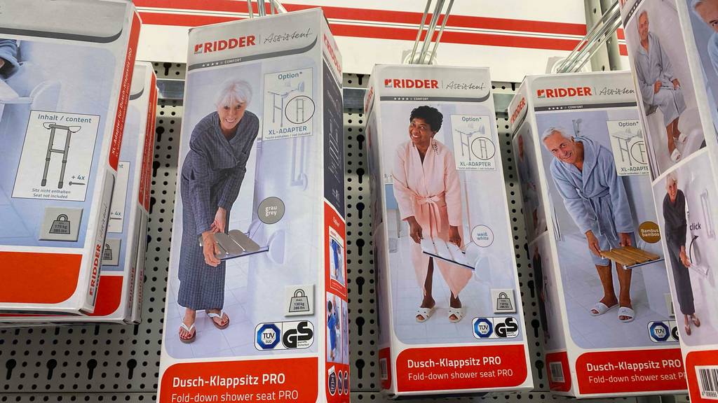 Mehrere Modelle in unterschiedlichen Farben von getesteten Duschklappsitzen von Ridder hängen in ihren Verpackungen an einem Verkaufsstand.