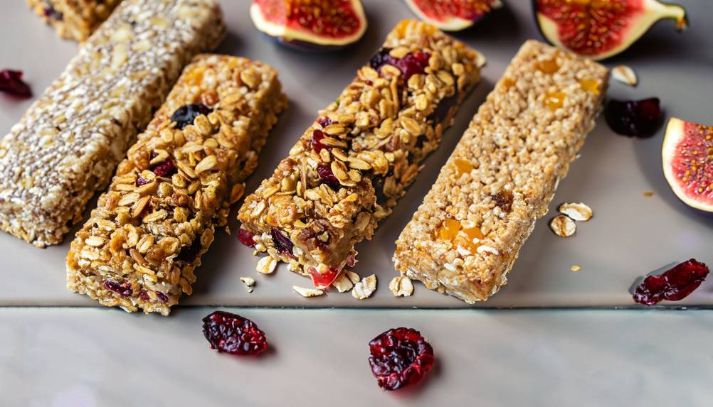 Müsliriegel, Feigen und getrocknete Cranberrys liegen auf einem Tisch.