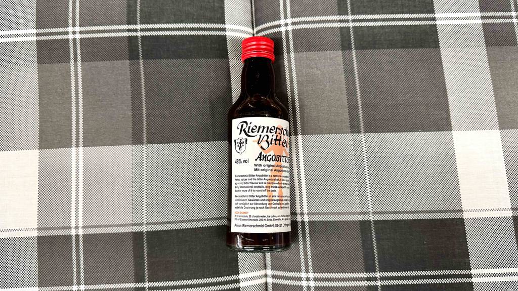 Eine Flasche getesteter Bitters liegt auf einer schwarz-weiß-karierten Decke.
