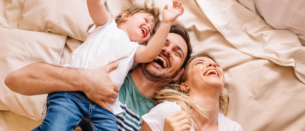 Riester-Rente im Test: Glückliche Familie liegt auf einem Bett.