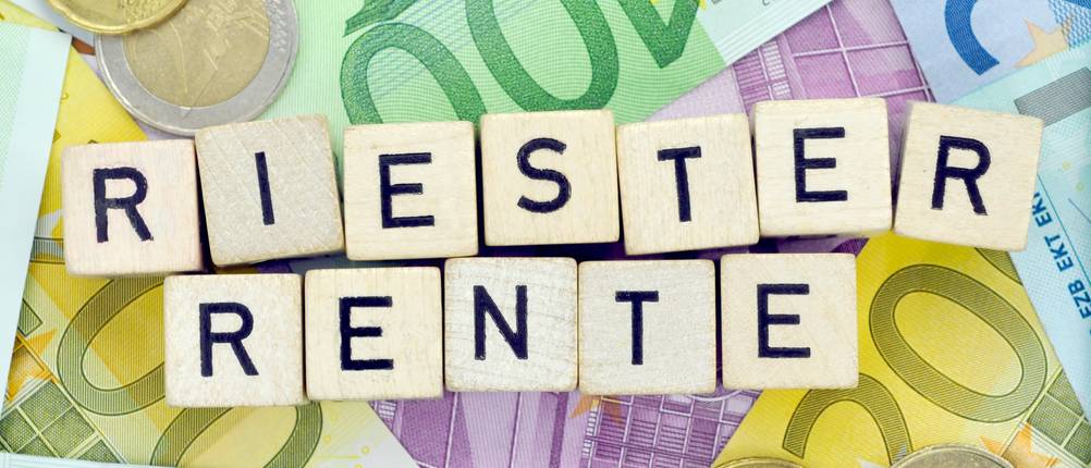 Riester-Rente im Test: Buchstabensteine liegen auf Bargeld und formen das Wort Riester-Rente