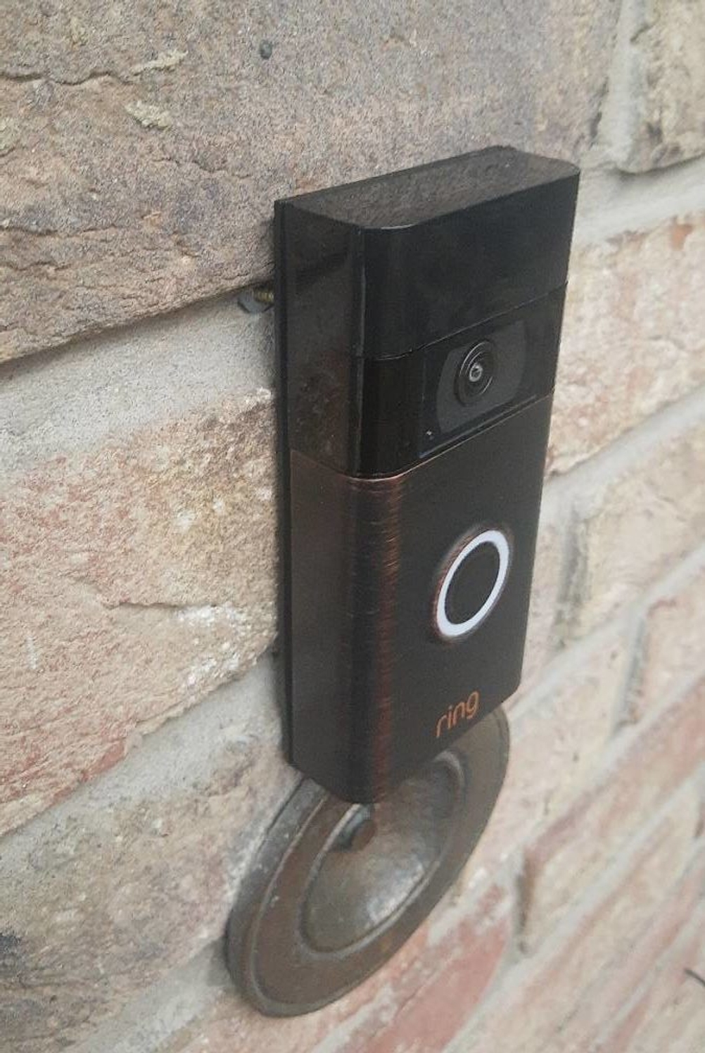 Eine schwarze Ring-Funkklingel im Test ist über einer Außenmauer-Klingel an einer Klinkerwand montiert.