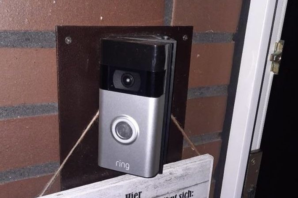 Getestete Funkklingel der Marke Ring verfügt über eine Kamera und ist in einem Klinkerwand-Eingangsbereich montiert oberhalb einer weißen Familientafel.