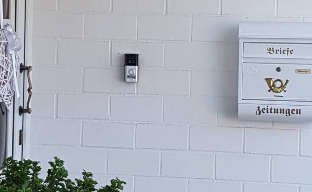 Video-Türsprechanlage im Test hängt an einer weißen Ziegel-Außenwand zwischen Haustür und Briefkasten.
