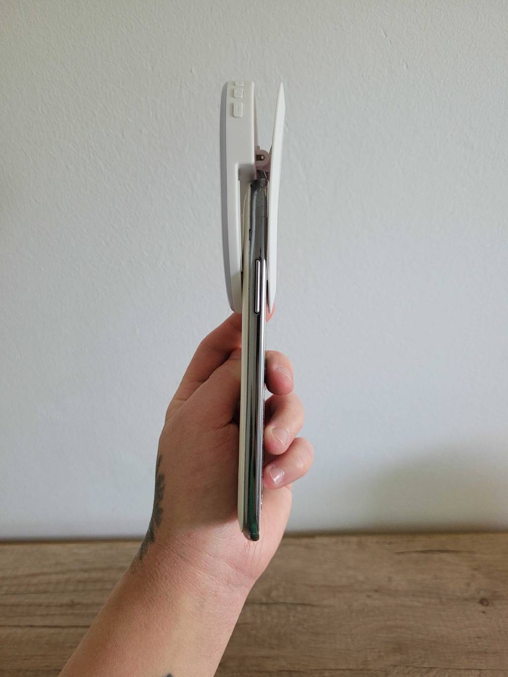 Ringlicht für das Handy getestet: Eine Hand hält ein Handy an dem ein Ringlicht befestigt ist seitlich vor eine helle Wand.