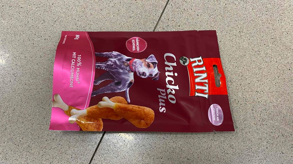 Getestetes Rinti-Hundefutter mit Hähnchen-Schenkel liegt in seiner 80-g-Verpackung auf dem Boden.