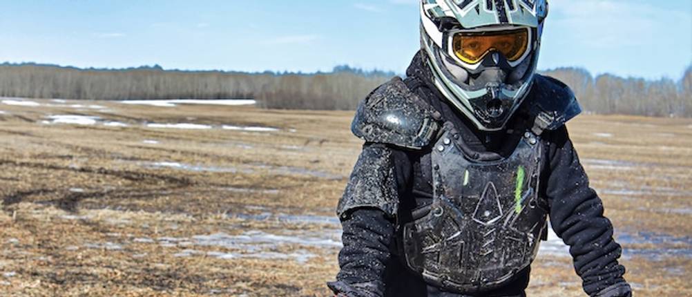 Rippenschutz im Test: Ein Endurofahrer steht mit Helm, Rippenschutz und Protektoren im Schlamm auf einer Wiese..