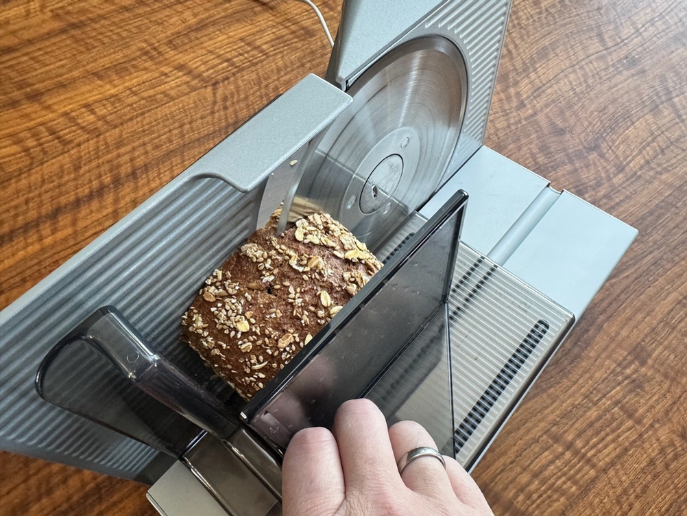 Eine Hand drückt das Brot während dem Schneiden mithilfe eines Aufsatzes gegen das Messer