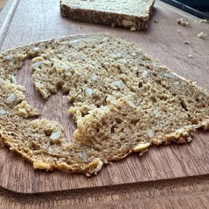 Eine hauchdünne, halb zerfallene Scheibe Vollkornbrot liegt auf einem Holzbrett