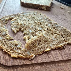 Eine hauchdünne, halb zerfallene Scheibe Vollkornbrot liegt auf einem Holzbrett