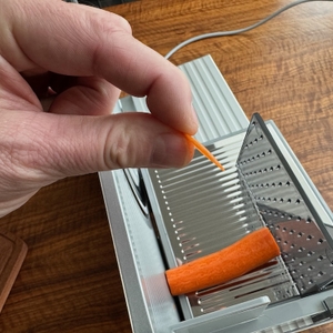 Eine Hand hält eine sehr dünne Karottenscheibe vor dem Ritter Serano 7 Duo Plus