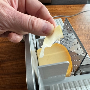 Eine Hand hält ein Stück Käse vor dem Ritter Serano 7 Duo Plus