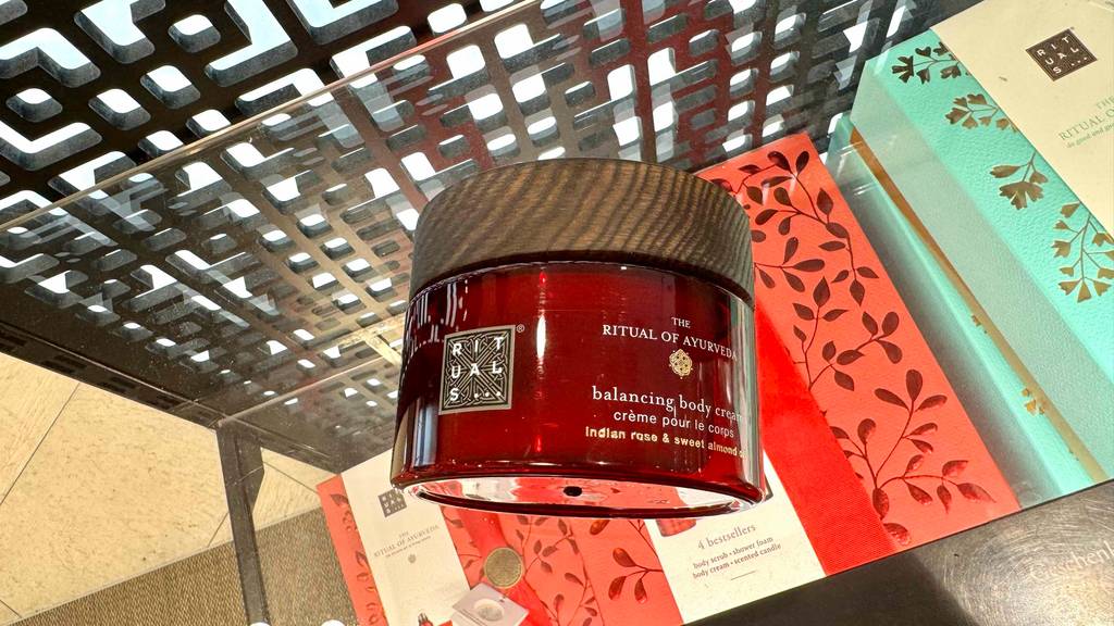 Ein Glasbehälter mit getesteter Rituals-Körpercreme liegt auf einer Glasfläche.