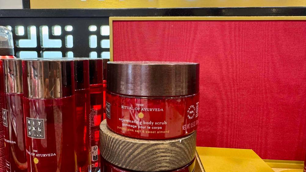 Neben anderen Produkten steht das Rituals-Peeling im Test vor einer roten Fläche.
